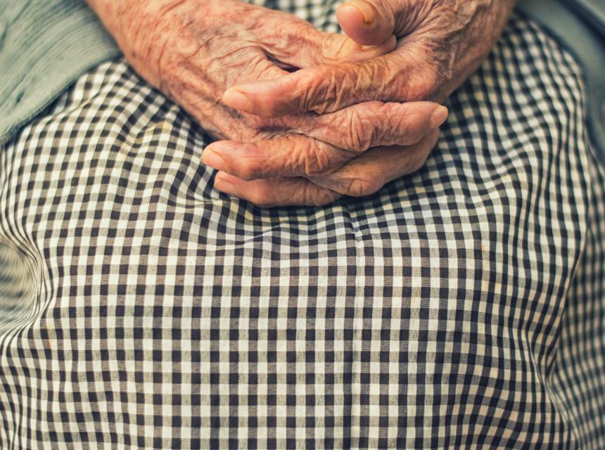 mani di donna anziana incrociate su un grembiule a piccoli quadretti